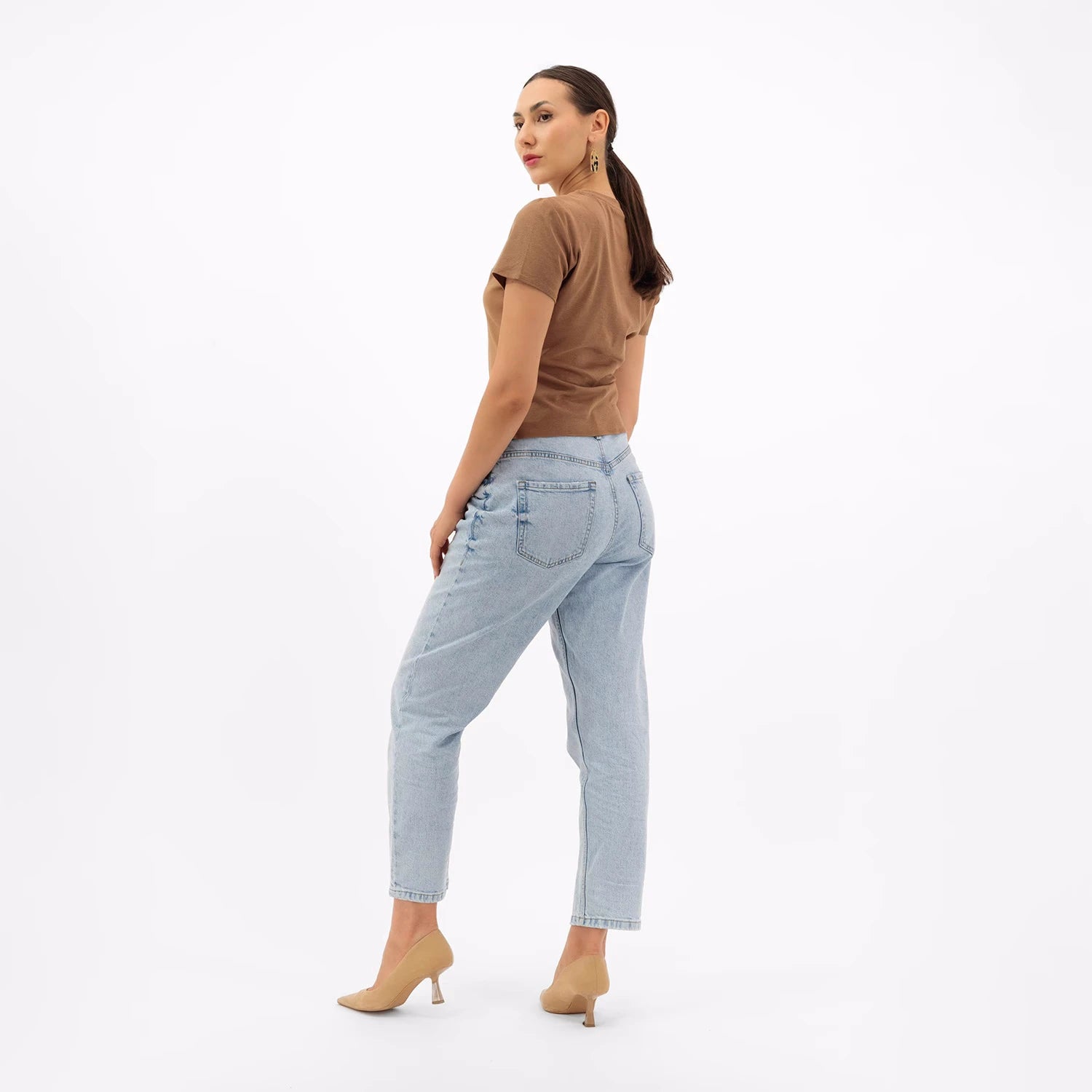 Woman wearing Caramel Melt t-shirt and light blue jeans with beige heels, posing from the back view on white background.