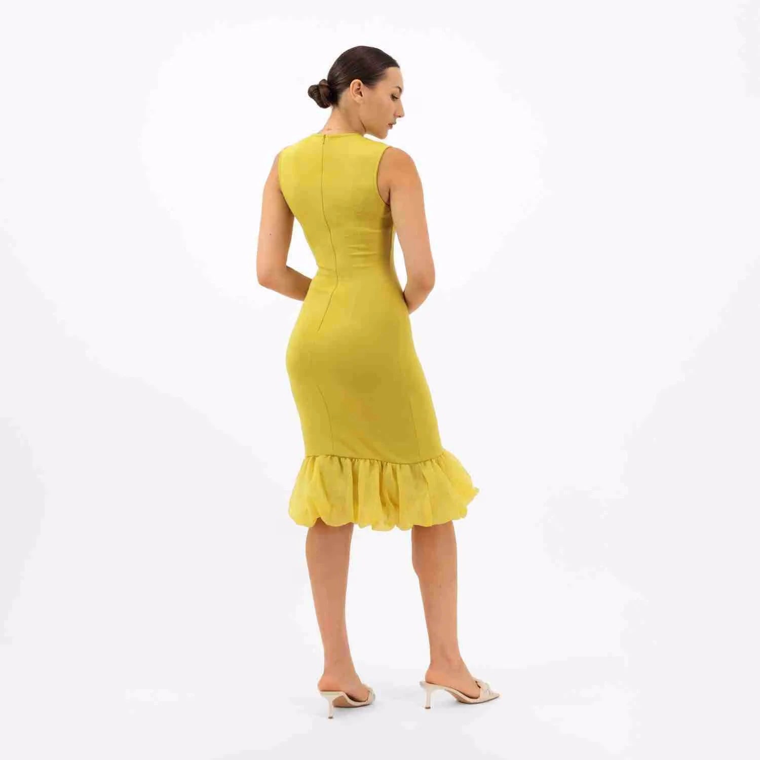 A woman wearing a luxury fitted yellow dress, designed with a stylish ruffled hem, photographed from the back.