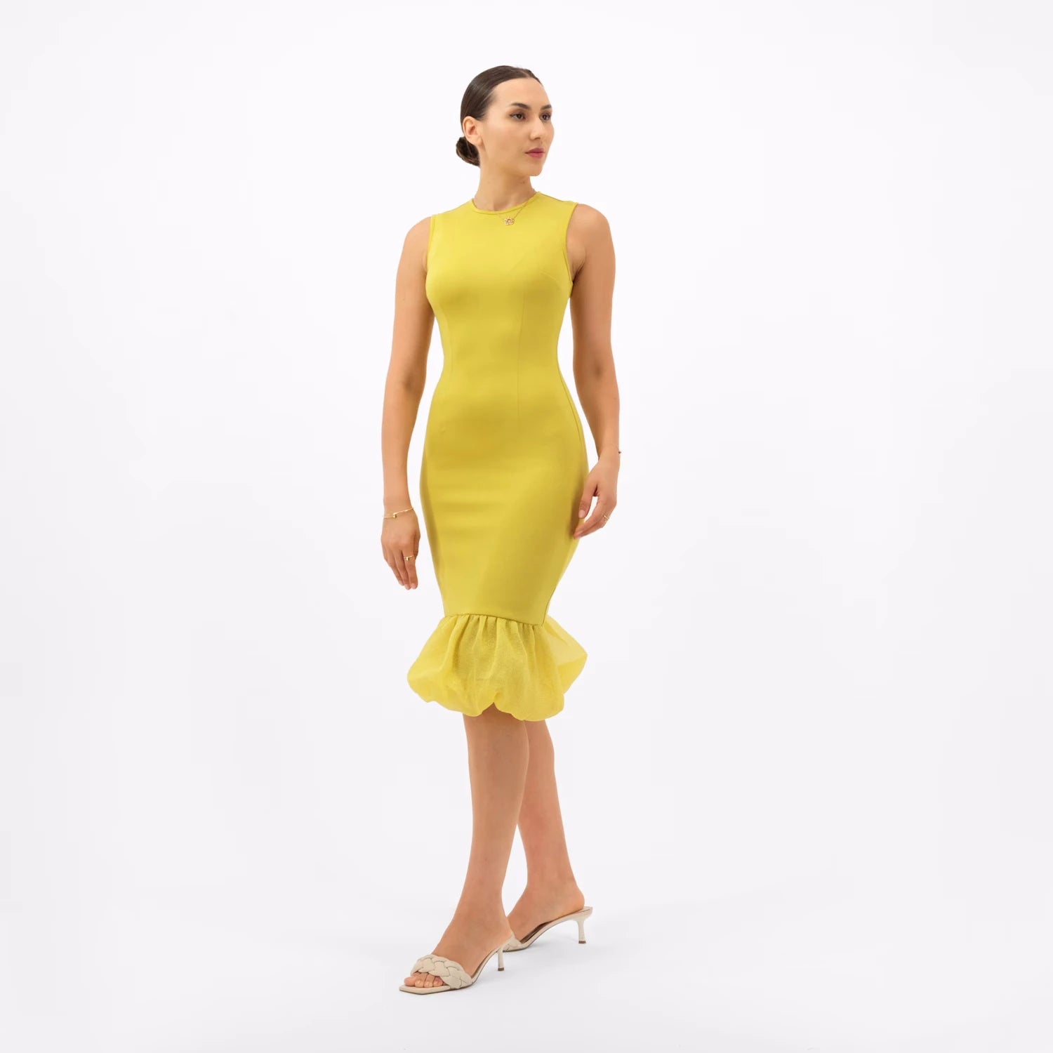 A woman modeling a form-fitting yellow-green dress with a ruffled hem, a chic luxury fashion look.