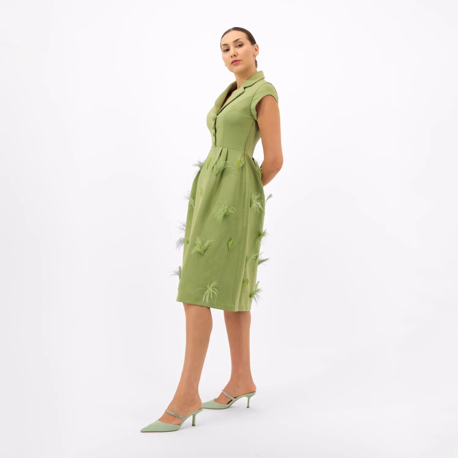 A woman in an old money style green dress with feather and leaf details.