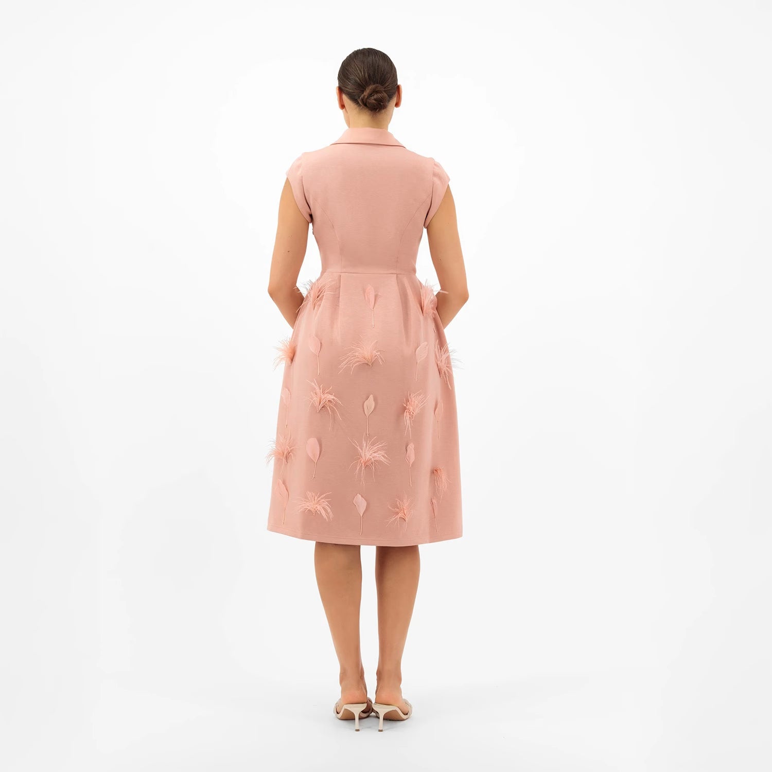 Woman wearing a pink dress with floral embroidery on a white background